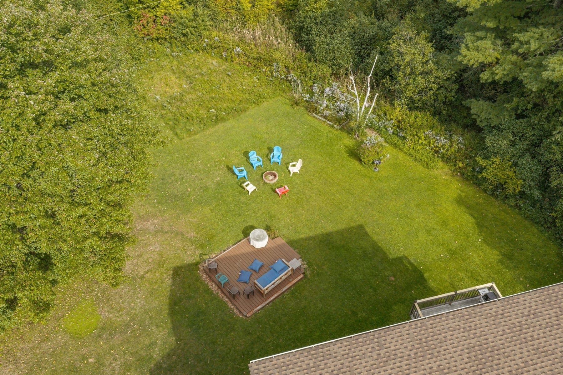 The back lawn from directly above: the fire pit, the freestanding deck, and the tree line