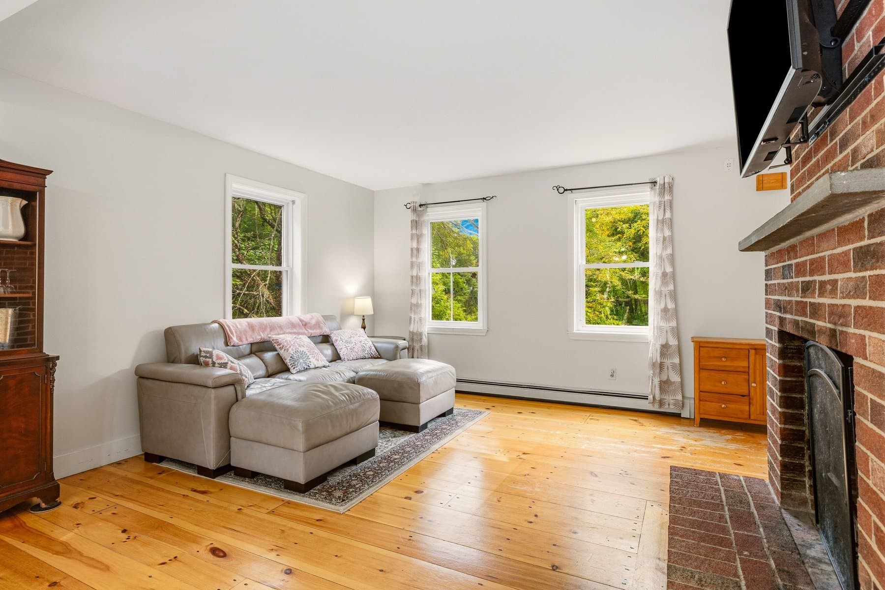 The sitting side of the living room with a sectional, 3 windows, and the fireplace